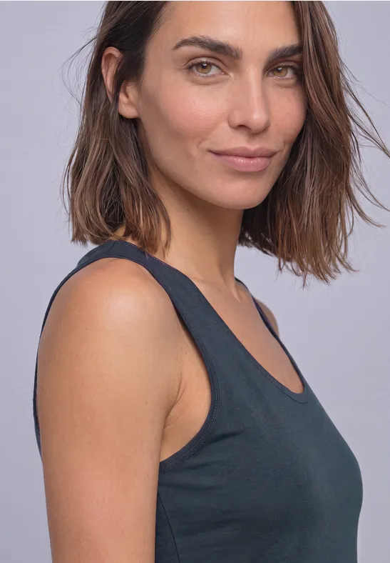 Porträt einer Frau mit schulterlangen braunen Haaren und schwarzem Top vor hellem Hintergrund.