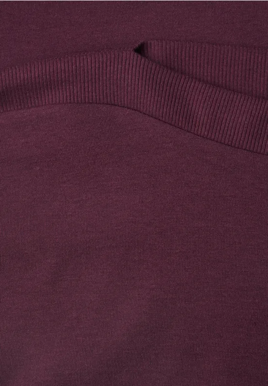 Nahaufnahme eines bordeauxroten Strickpullovers mit Rippstrickbündchen.