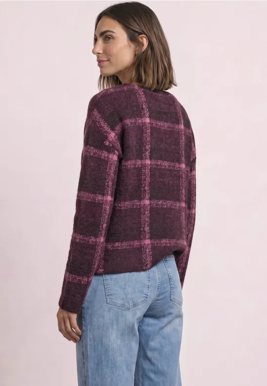 Frau von der Seite mit lila kariertem Pullover und blauen Jeans.