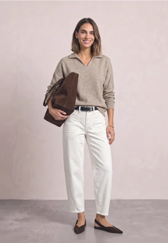 Frau in beigem Pullover, weißer Hose, schwarzem Gürtel, brauner Tasche und flachen Schuhen.