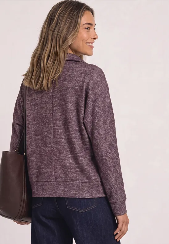 Eine Frau in lila Pullover mit Tasche, von hinten gesehen.