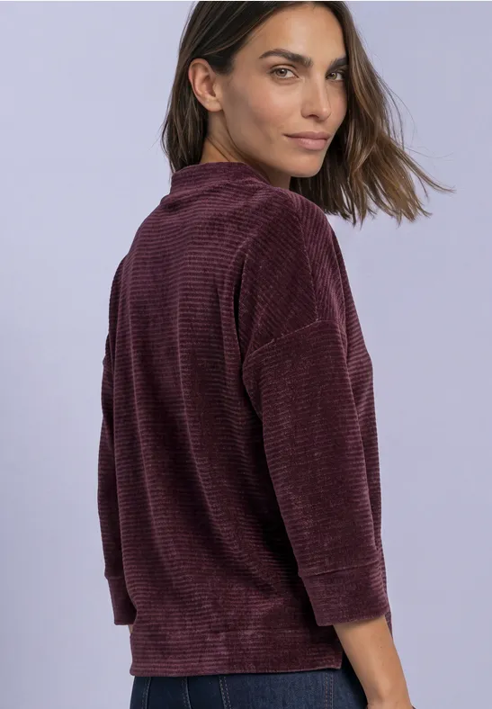 Vrouw in bordeauxrood corduroy shirt met driekwart mouwen, kijkt over haar schouder heen.