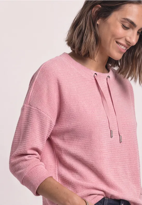 Frau in einem rosa Pullover, die lächelnd zur Seite blickt.