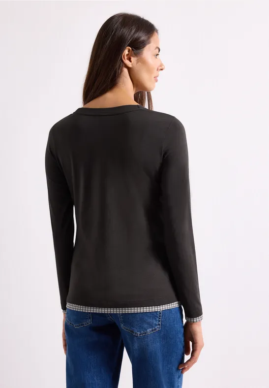 Frau von hinten in schwarzem Langarmshirt mit gesprenkeltem Saum und blauen Jeans
