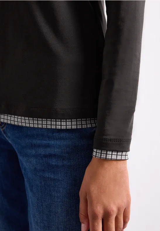 Teilansicht einer Person mit schwarzem Langarmshirt über kariertem Hemd und blauer Jeans.