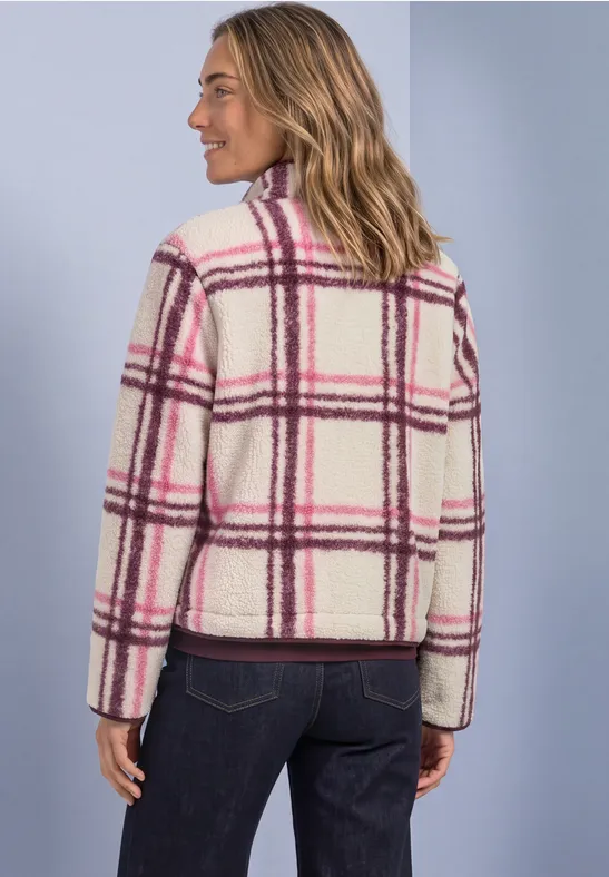 Vrouw draagt witte, zachte geruite jas met roze-paarse strepen, zijaanzicht tegen lichtblauwe achtergrond.