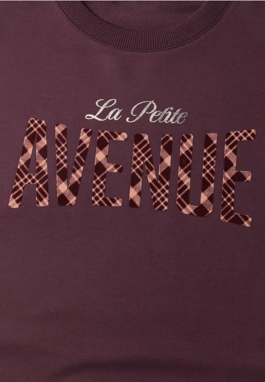 Dunkelrotes T-Shirt mit Schriftzug 'La Petite AVENUE' in karierter Optik.