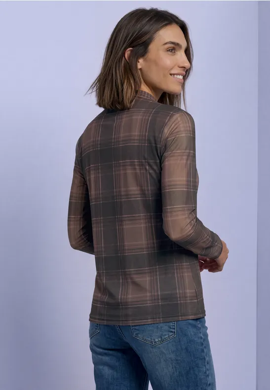Frau trägt kariertes Langarmshirt und Jeans, steht vor hellem Hintergrund, von hinten.