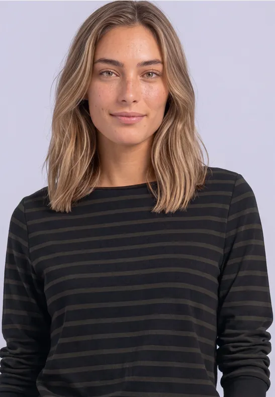 Junge Frau mit schulterlangen, hellbraunen Haaren und einem schwarz-oliv gestreiften Langarmshirt vor hellem Hintergrund.