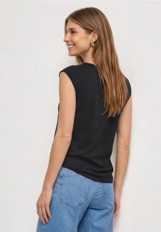 Vrouw van achteren in zwart topje en blauwe spijkerbroek voor neutrale achtergrond.