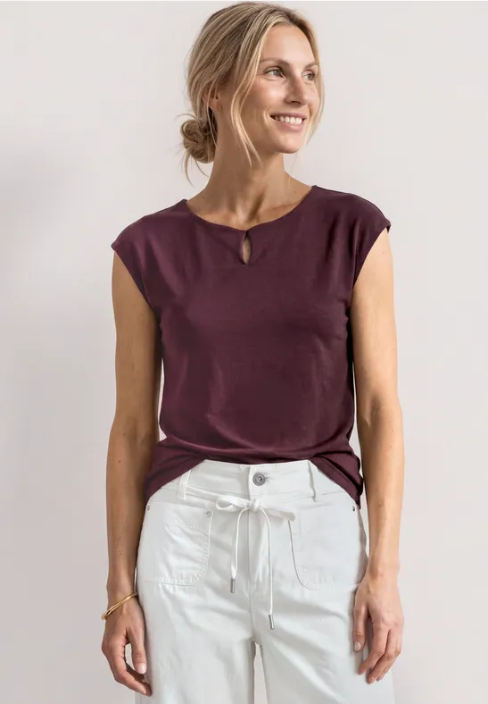 Vrouw in bordeaux mouwloos shirt en witte high waist-jeans voor een lichte achtergrond