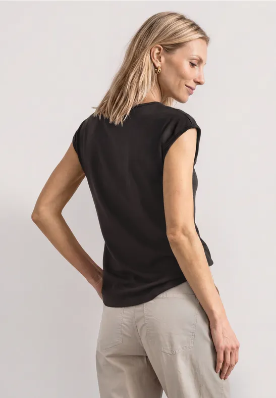 Vrouw in zwart T-shirt en beige broek, van achteren gefotografeerd.
