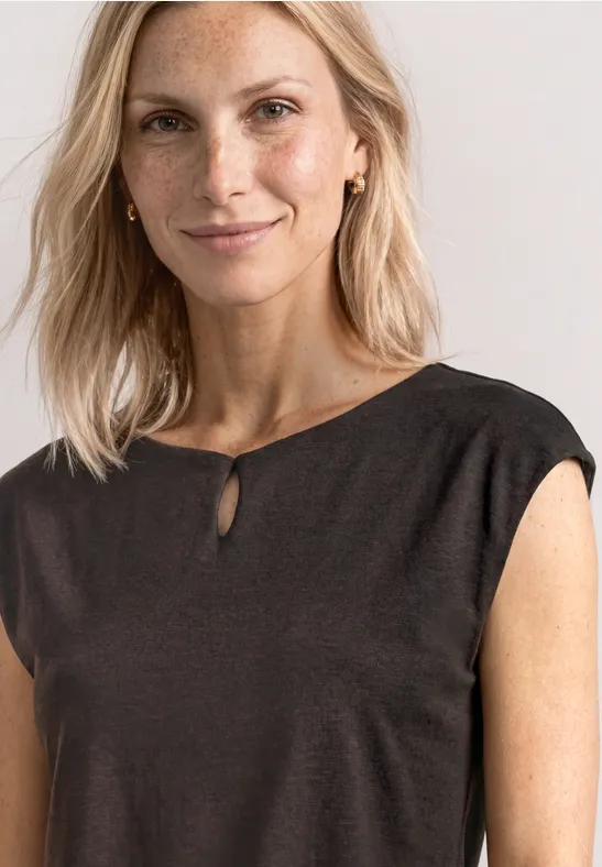 Vrouw in mouwloze zwarte blouse met kleine split bij de hals voor een neutrale achtergrond.