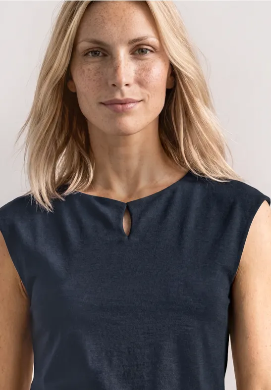 Femme aux cheveux blonds mi-longs porte un haut sans manches bleu foncé avec une petite fente au col.