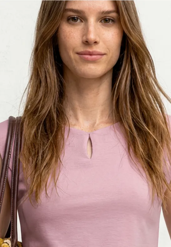 Femme en haut rose avec découpe à l'encolure, sac marron à l'épaule, cheveux longs bruns, fond blanc