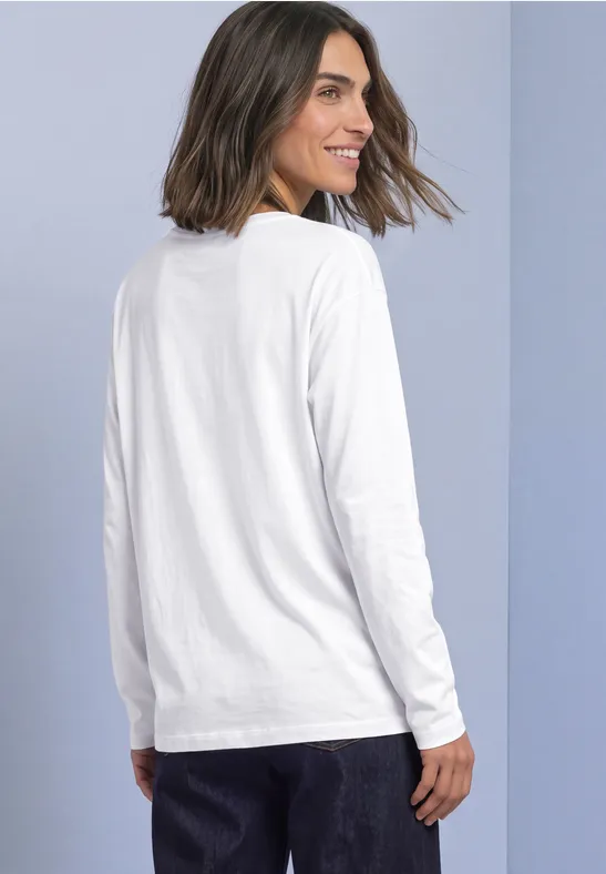 Vrouw met halflang haar draagt een wit T-shirt met lange mouwen, staat in zijzicht en kijkt over haar schouder.