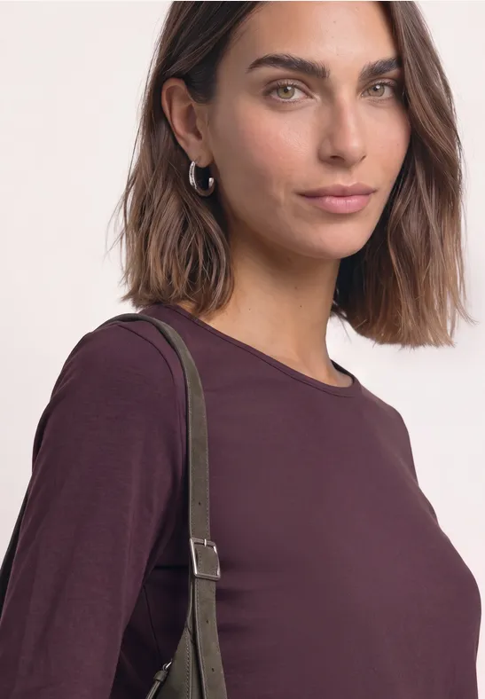 Portret van een vrouw met een bordeauxkleurige top met lange mouwen en een groene schoudertas.