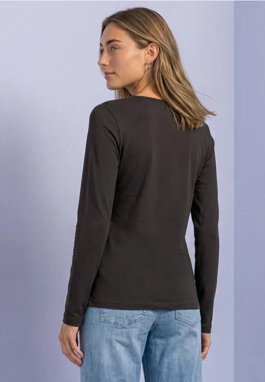 Vrouw van achteren, zwarte lange mouw top en jeans, lichtblauwe achtergrond.