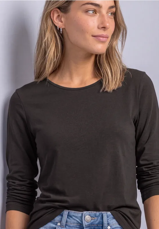 Een vrouw draagt een zwart, eenvoudig shirt met lange mouwen tegen een neutrale achtergrond.