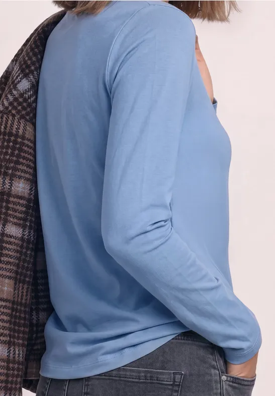 Zijaanzicht van een persoon in een lichtblauw shirt met lange mouwen en een ruitjas nonchalant over de schouder.