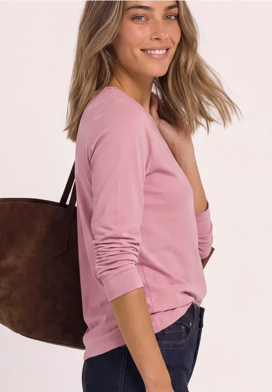 Frau in rosa Langarmshirt mit brauner Schultertasche lächelt seitlich in die Kamera.