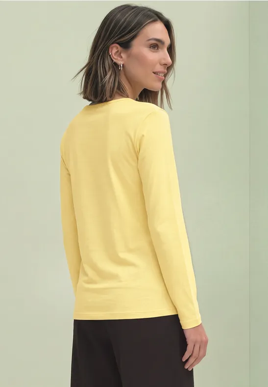 Frau von der Seite in gelbem Langarmshirt vor hellgrünem Hintergrund.