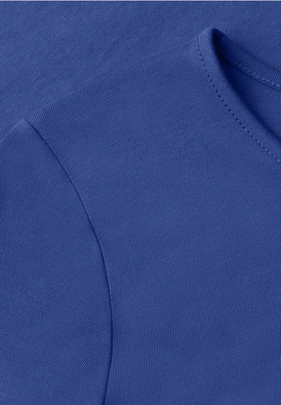 Nahaufnahme eines einfarbigen blauen T-Shirts mit Rundhalsausschnitt und Naht am Ärmelansatz.