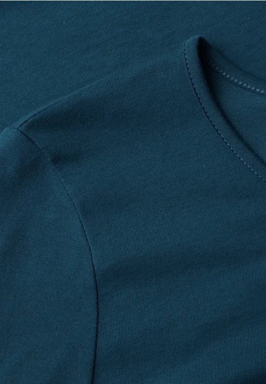Dunkeltürkises T-Shirt aus Baumwollstoff, Detailaufnahme von Ärmel und Halsausschnitt.