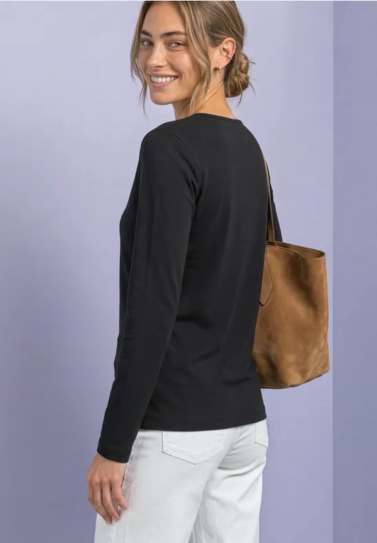 Une junge femme souriante porte un t-shirt noir, un jean blanc et un sac brun sur fond violet.