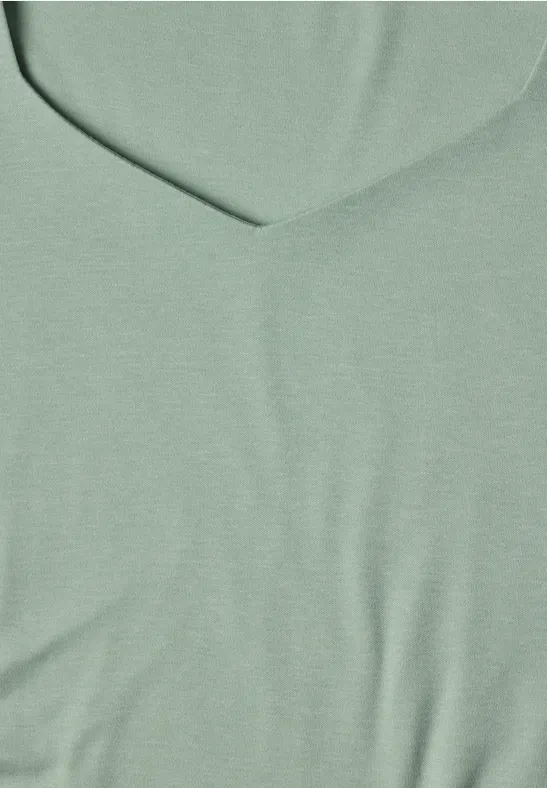Gros plan sur un tissu vert clair à col en V, texture fine et uniforme.