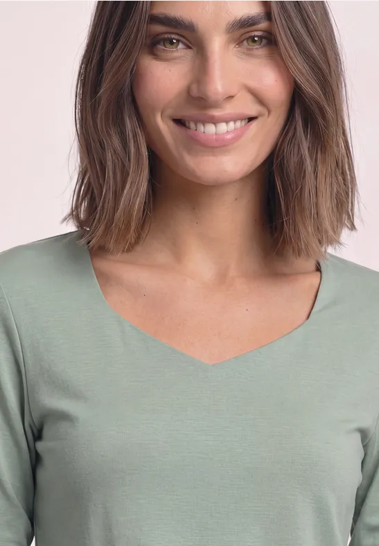 Une femme souriante aux cheveux bruns portant un haut vert à encolure en V.