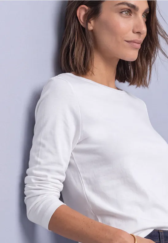 Zijaanzicht van een vrouw in een wit shirt met lange mouwen voor een lichte achtergrond.