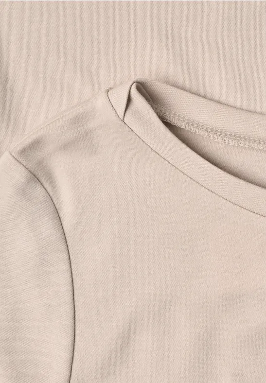 Nahaufnahme eines beigen T-Shirts mit rundem Ausschnitt und feiner Nahtführung.