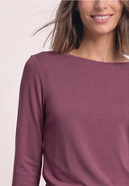 Frau trägt ein langärmeliges, pflaumenfarbenes Shirt mit Boot-Ausschnitt.