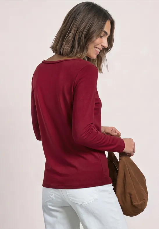 Femme vue de dos portant un pull rouge, un pantalon blanc et un sac marron.