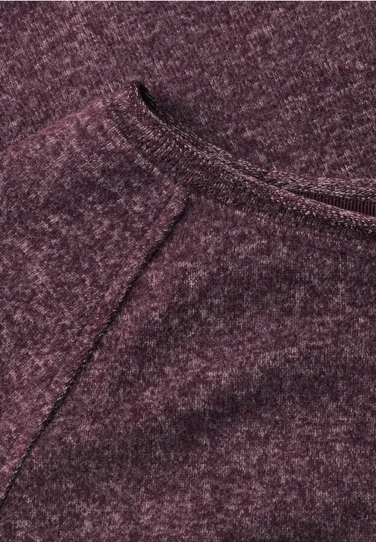 Nahaufnahme eines bordeauxfarbenen Strickstoffs mit sichtbarer Naht und weicher, melierter Textur.