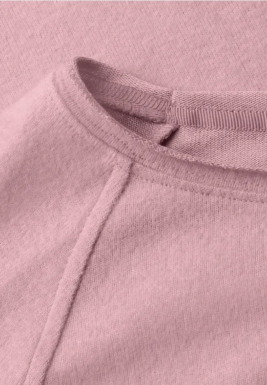 Nahaufnahme eines rosa Fleece-Oberteils mit sichtbarer Naht am Rundhalsausschnitt.