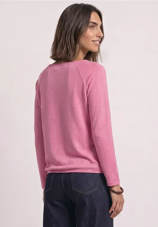 Eine Frau in rosa Pullover und blauer Jeans schaut über ihre Schulter.
