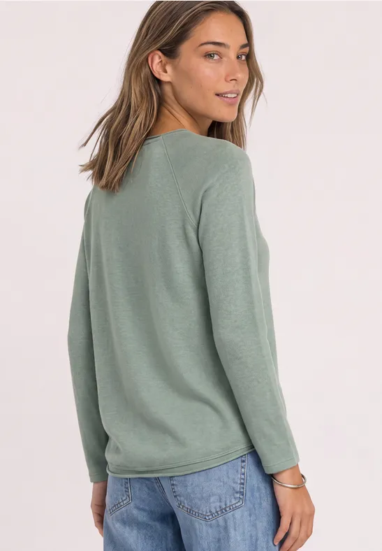 Frau in langärmeligem grünen Pullover und Jeans schaut über die Schulter.