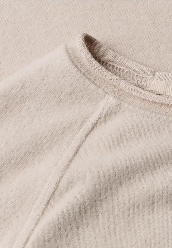 Nahaufnahme eines beigen Pullovers aus weichem Stoff mit Rundhalsausschnitt und sichtbarer Naht.