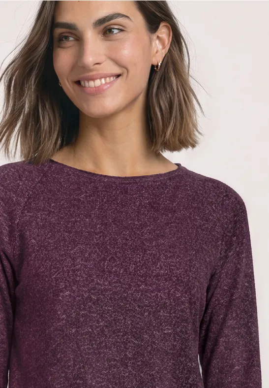 Een vrouw met halflang haar draagt een paarse trui en lacht zachtjes.