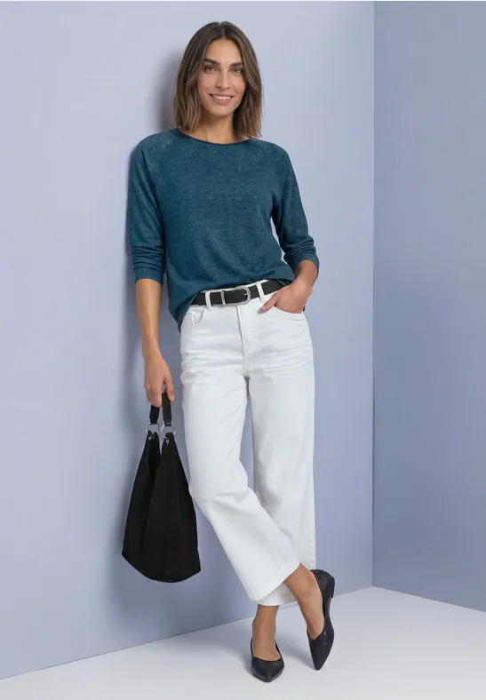 Vrouw in stoere casual look: groen shirt, witte wijde broek, zwarte ballerina’s en grote schoudertas.