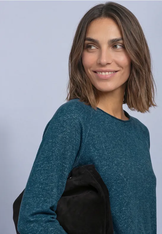 Een vrouw in een groenblauwe trui lacht terwijl ze opzij kijkt.