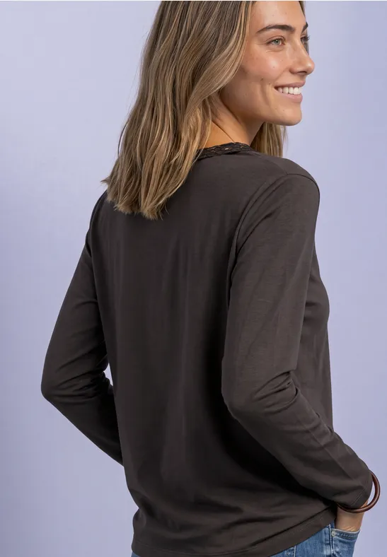Junge Frau im Profil, lächelnd, in dunklem Langarmshirt vor hellem lila Hintergrund.