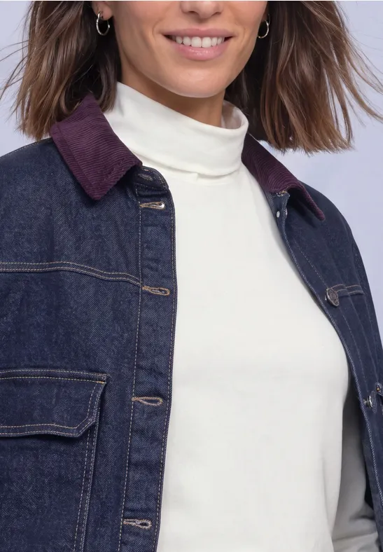 Eine Frau trägt eine dunkle Jeansjacke mit burgunderfarbenem Kragen und einen weißen Rollkragenpullover.