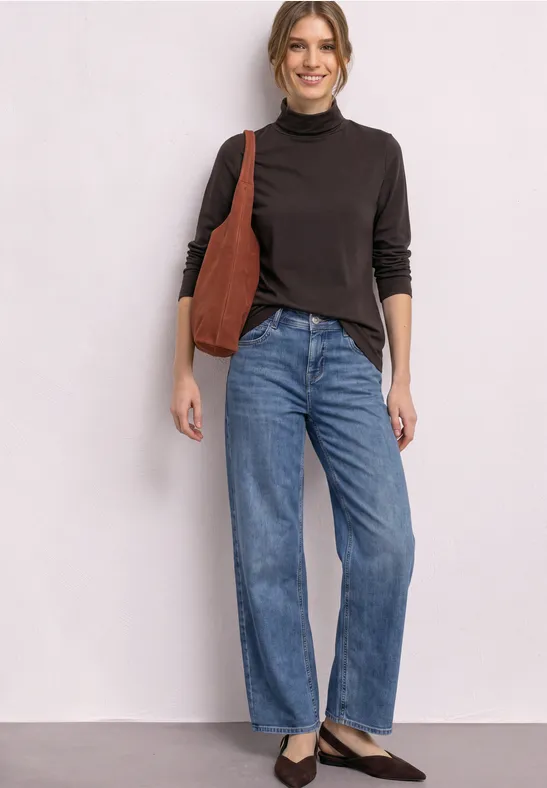 Frau mit schwarzem Rollkragen, blauen Straight-Jeans und brauner Schultertasche.