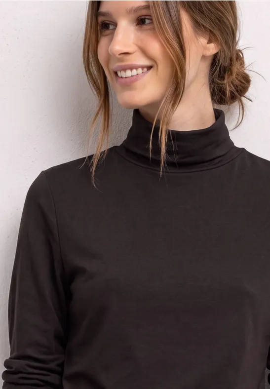 Junge Frau lächelnd in schwarzem Rollkragenpullover vor hellem Hintergrund.