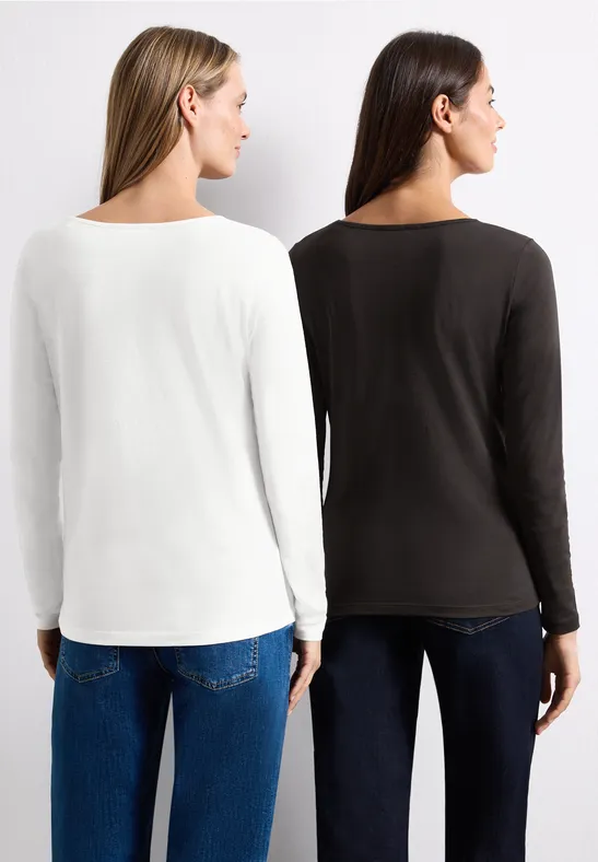 Zwei Frauen von hinten in langen Shirts (weiß und dunkel) mit Jeans, vor neutralem Hintergrund.