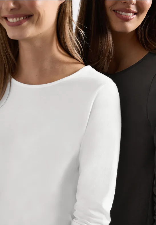 Zwei Frauen tragen schlichte Langarmshirts in Weiß und Schwarz.