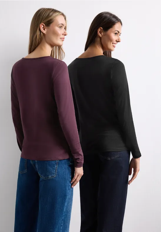 Zwei Frauen stehen nebeneinander, Rücken zur Kamera, in lila und schwarzem Langarmshirt und Jeans.